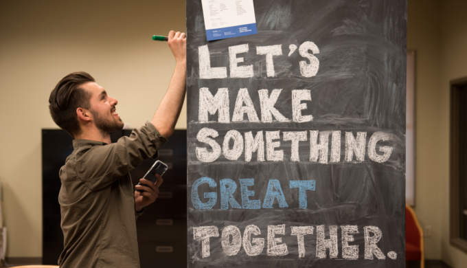 Smiling student writing on chalkboard that says "Let's Make Something Great Together."